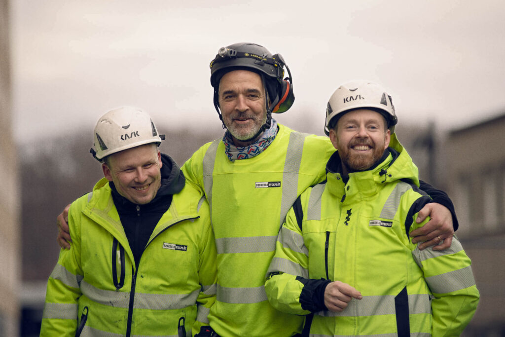 Tre arbeidere på byggeplass samarbeider om digital arbeidsordre.